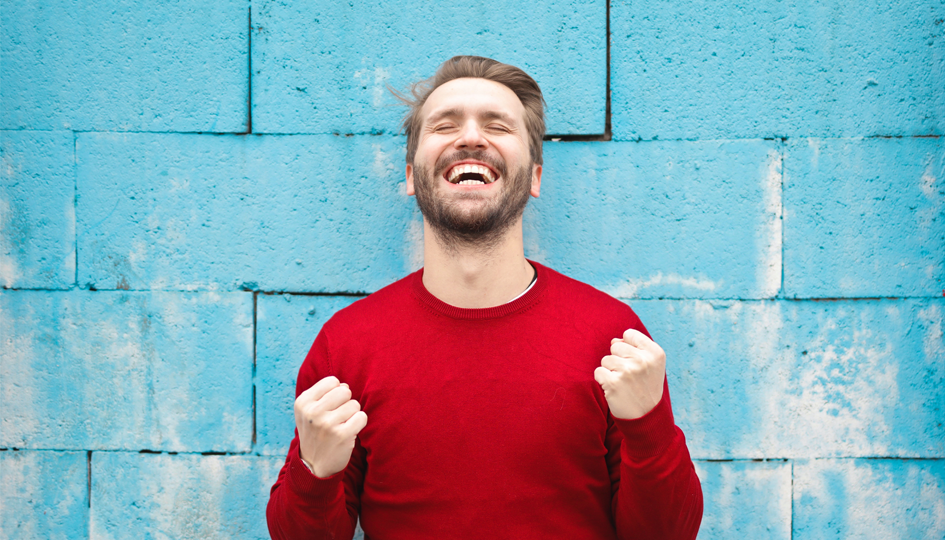 Happy Man in a red sweater up against a blue wall | Employee Recommended Workplace | Benefits by Design