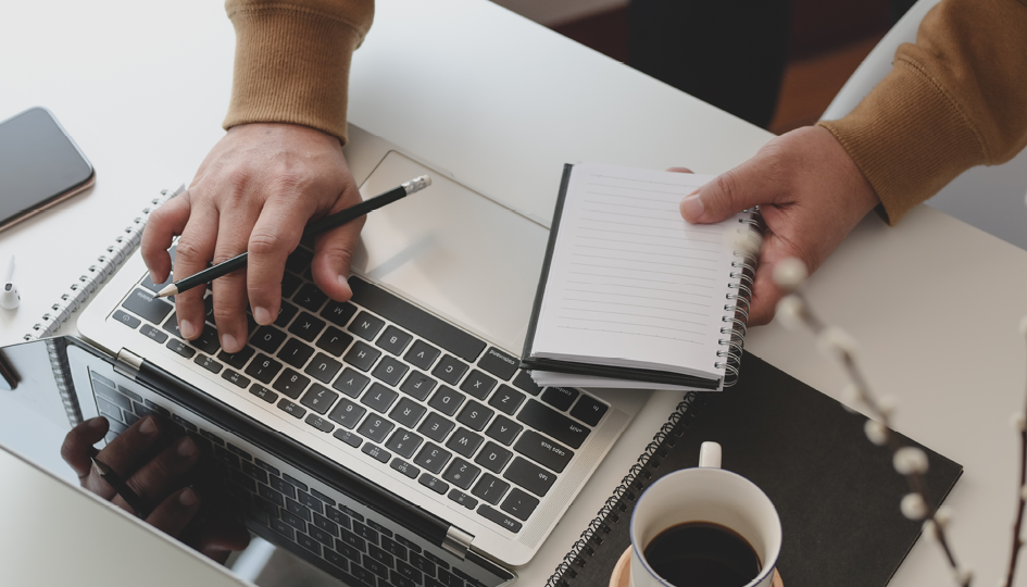 Man with notepad typing on computer | Online Enrollment } Benefits by Design