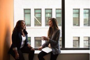 Two women talking next to a large window fostering best practices for optimal employee health
