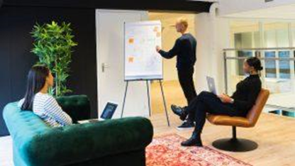 Three people having a meeting about designing a workspace for optimal employee health in a meeting room with a black wall and a large plant