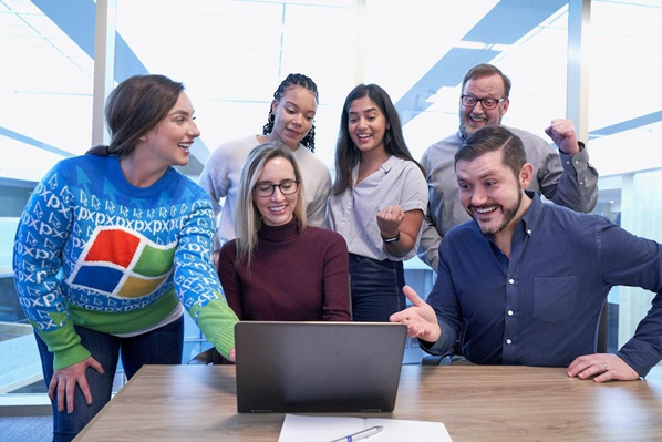 group of excited employees standing around a laptop at a desk