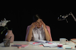 A seemingly sad woman in a pink blazer looking at her desk.