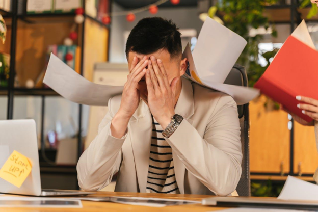 Stressed man at work surrounded by papers.